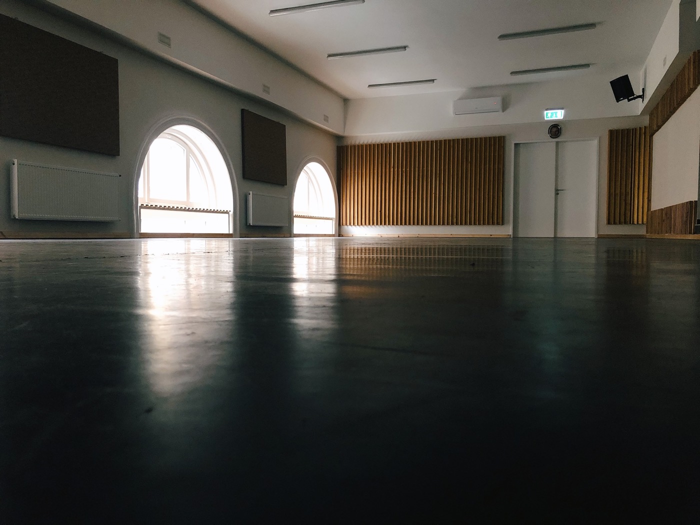A refurbished high-ceilinged hall with a reflective concrete floor, arched windows and a timber-battened wall.